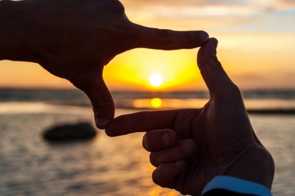 Person's hand's framing a sunset