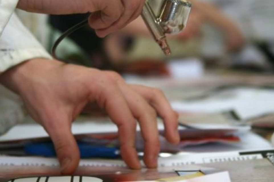 Detail of a student airbrushing in a school classroom.