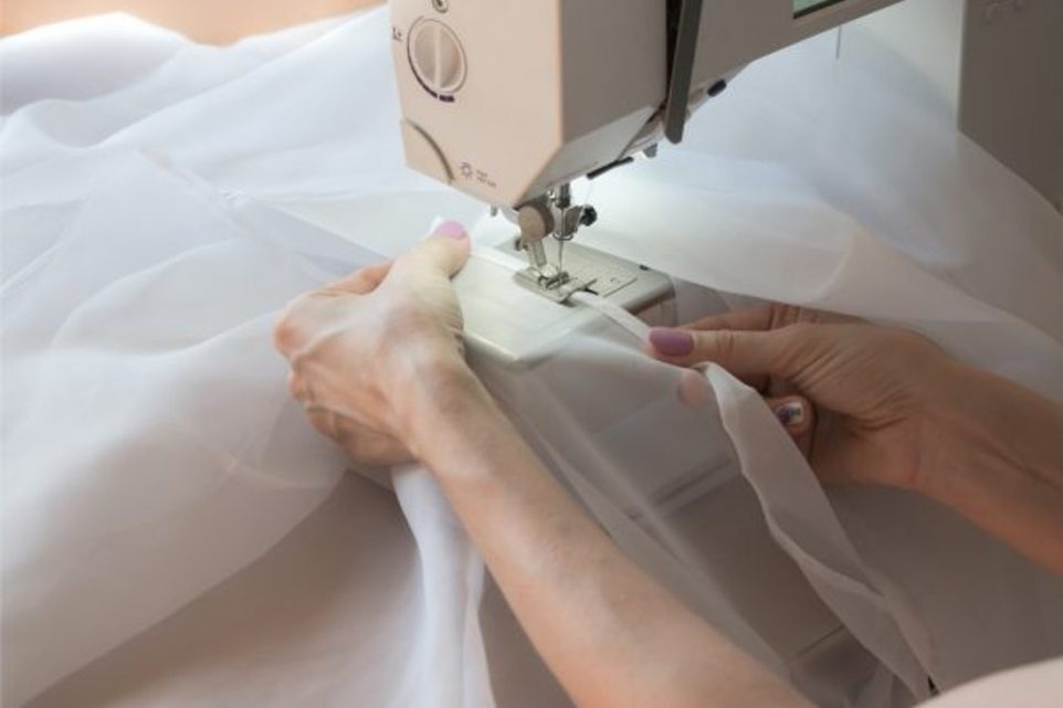 Woman using a sewing machine on white curtains