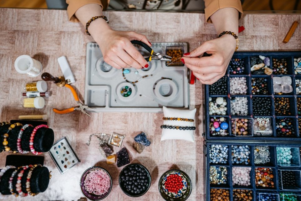 Young woman making jewelry with beads in her home.